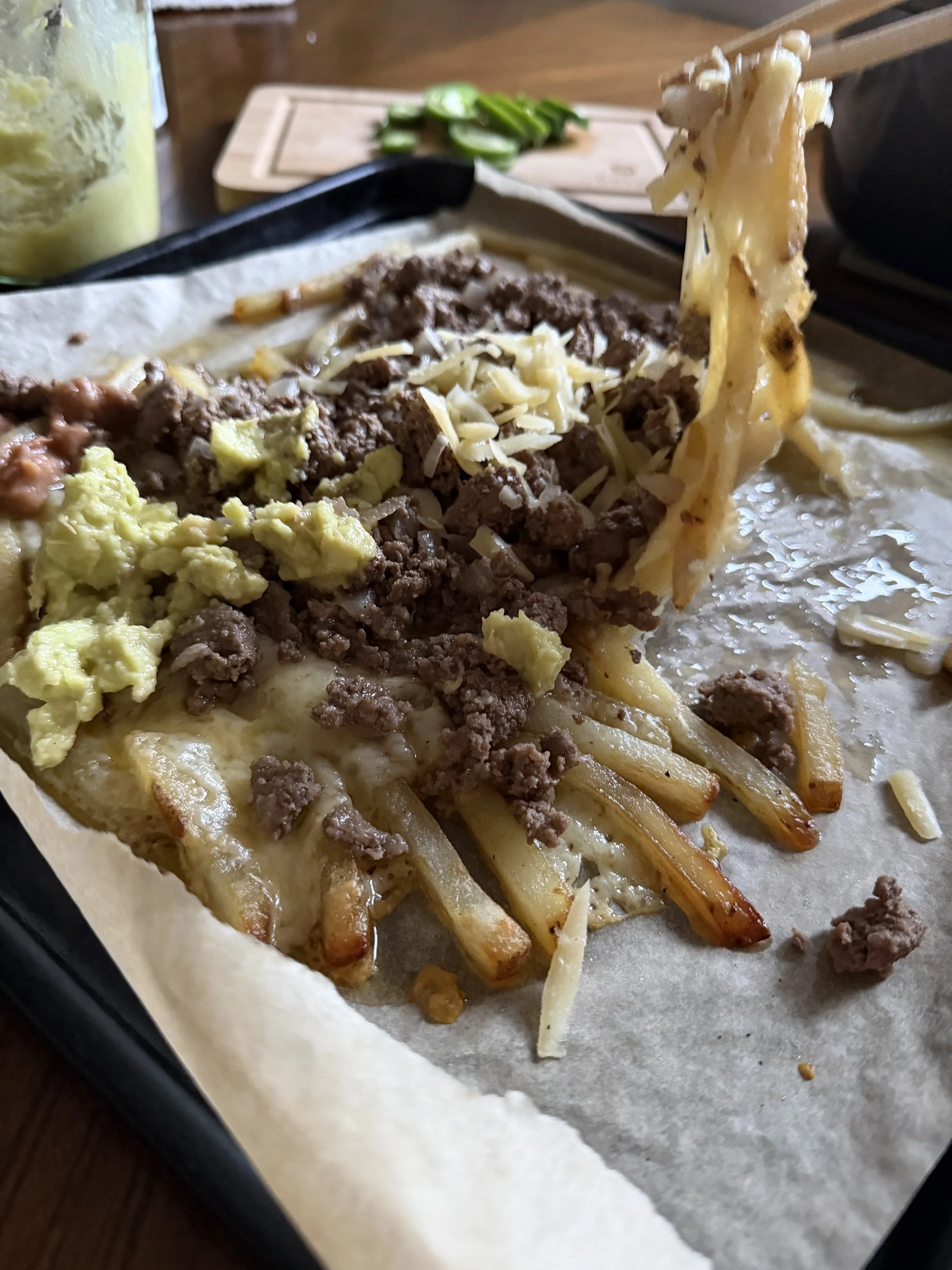 Carne asada fries with melted cheese being lifted with chopsticks, showing a stretchy cheese pull over crispy tallow fries and seasoned ground beef.