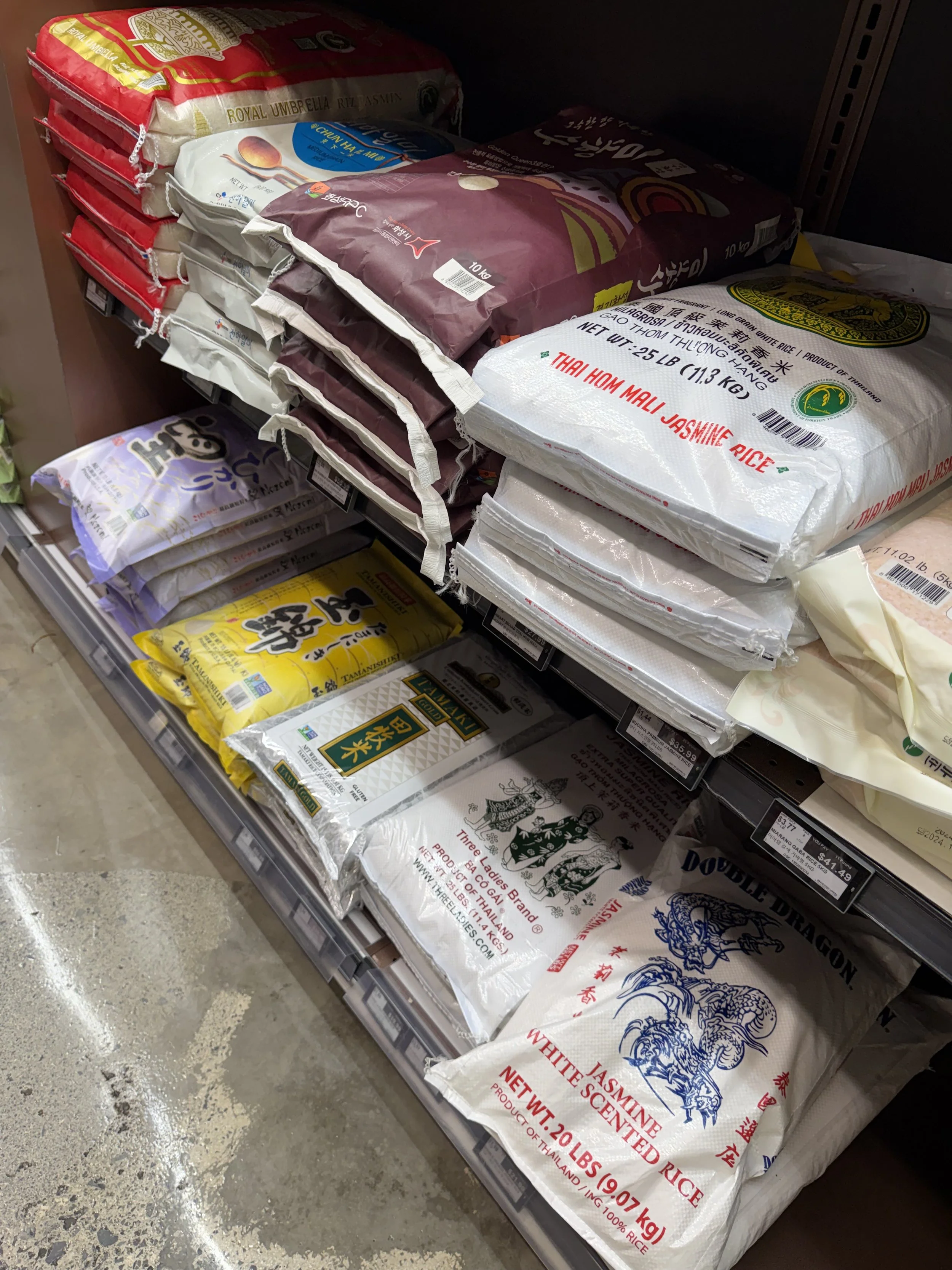 Piles of white rice bags at Asian H Mart grocery store showing various conventional rice options