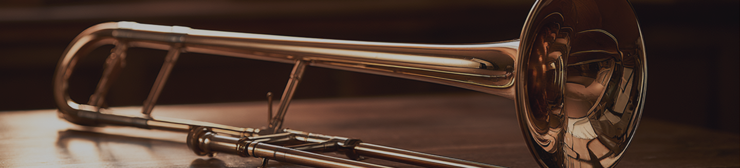 A shiny, brass trumpet lying on a wooden surface with a dark background.