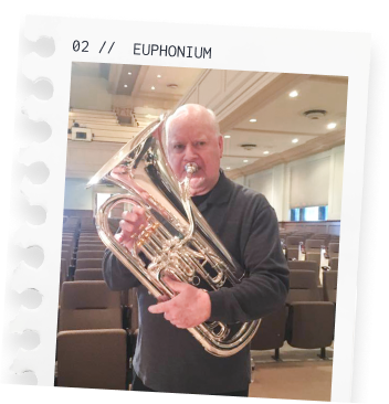 Man with a fierce expression holding a brass euphonium in a room with theater-style seating.
