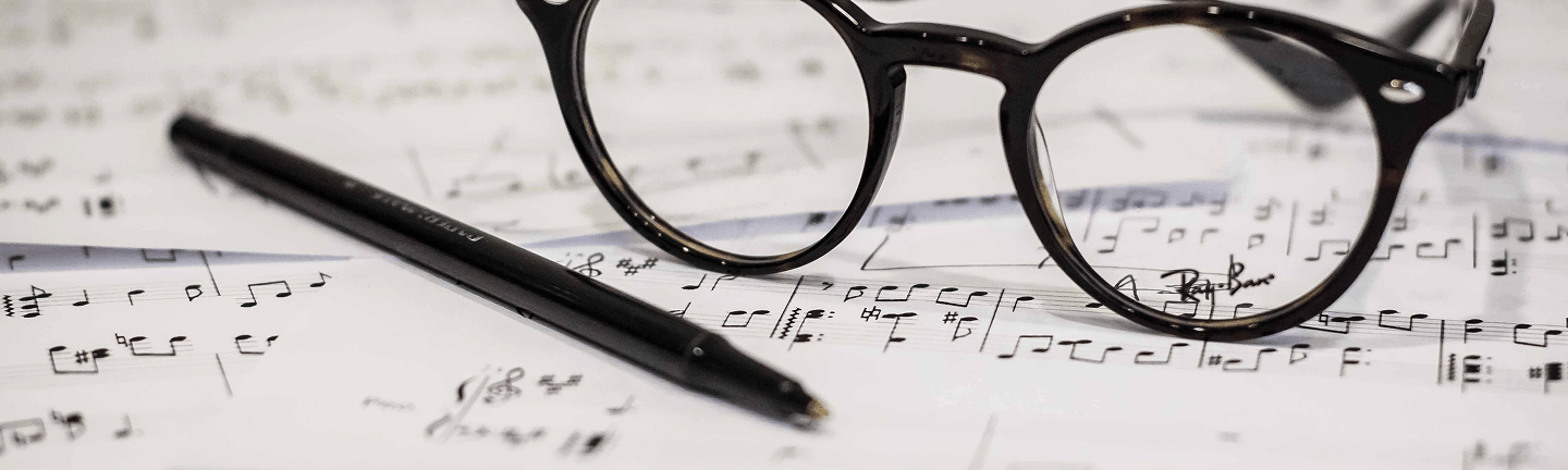 A pair of black glasses and a black pen resting on sheet music.