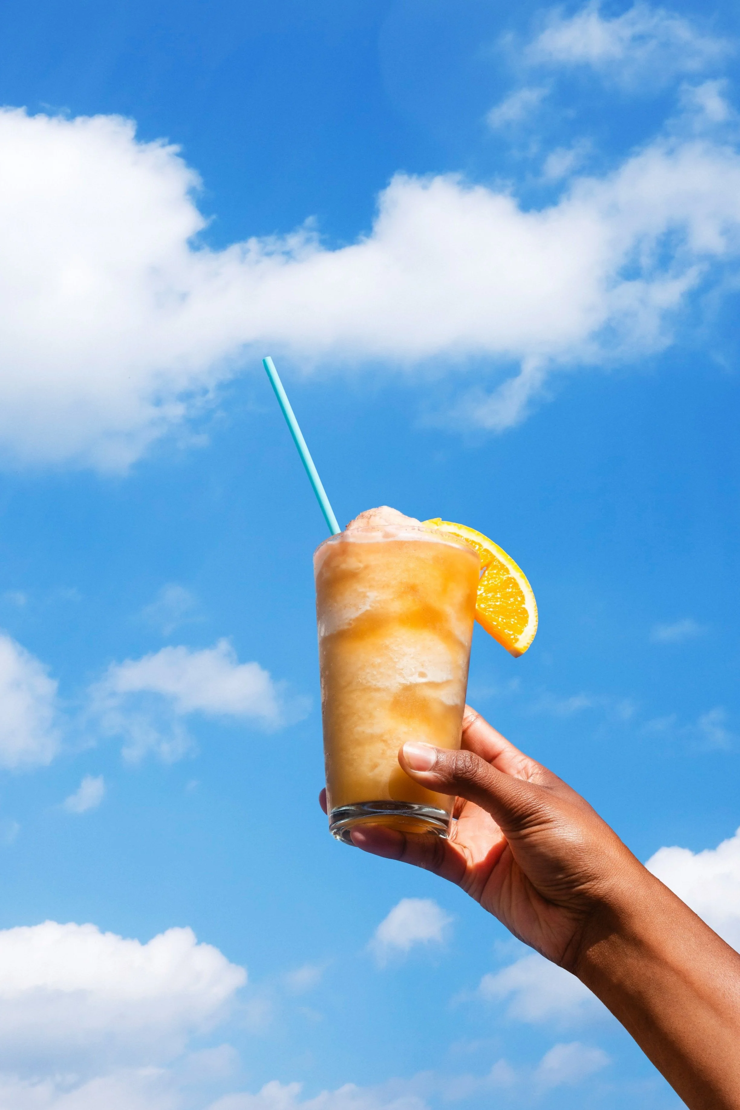 Product photo of orange slushie against sunny sky background with clouds for local coffee shop
