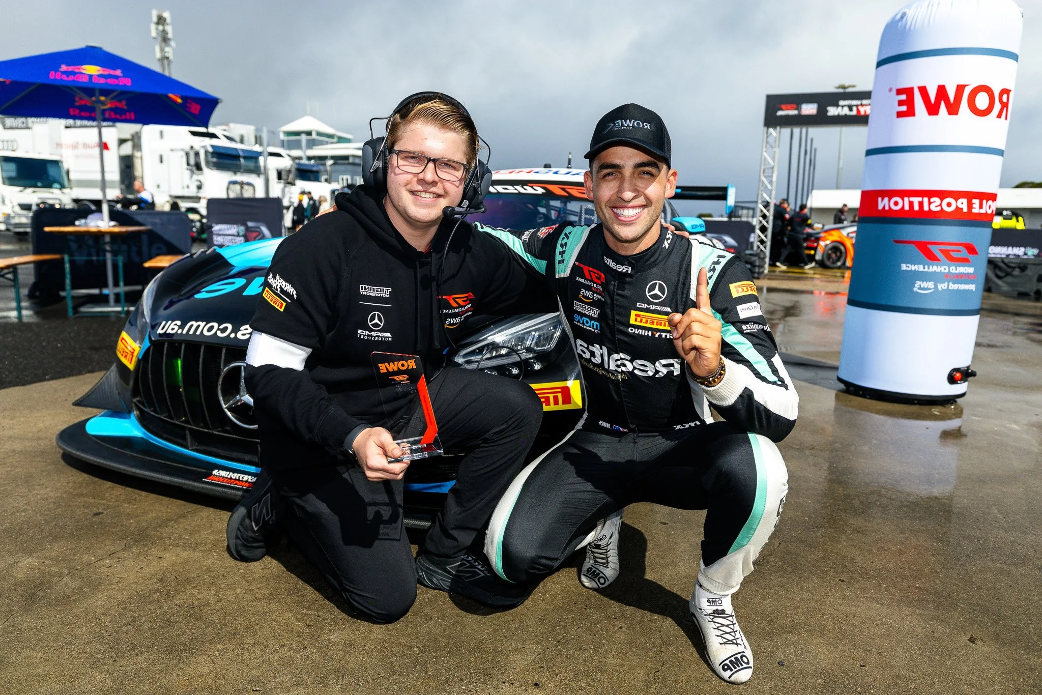 Race car driver in helmet and racing suit celebrating by a parked race car at night.