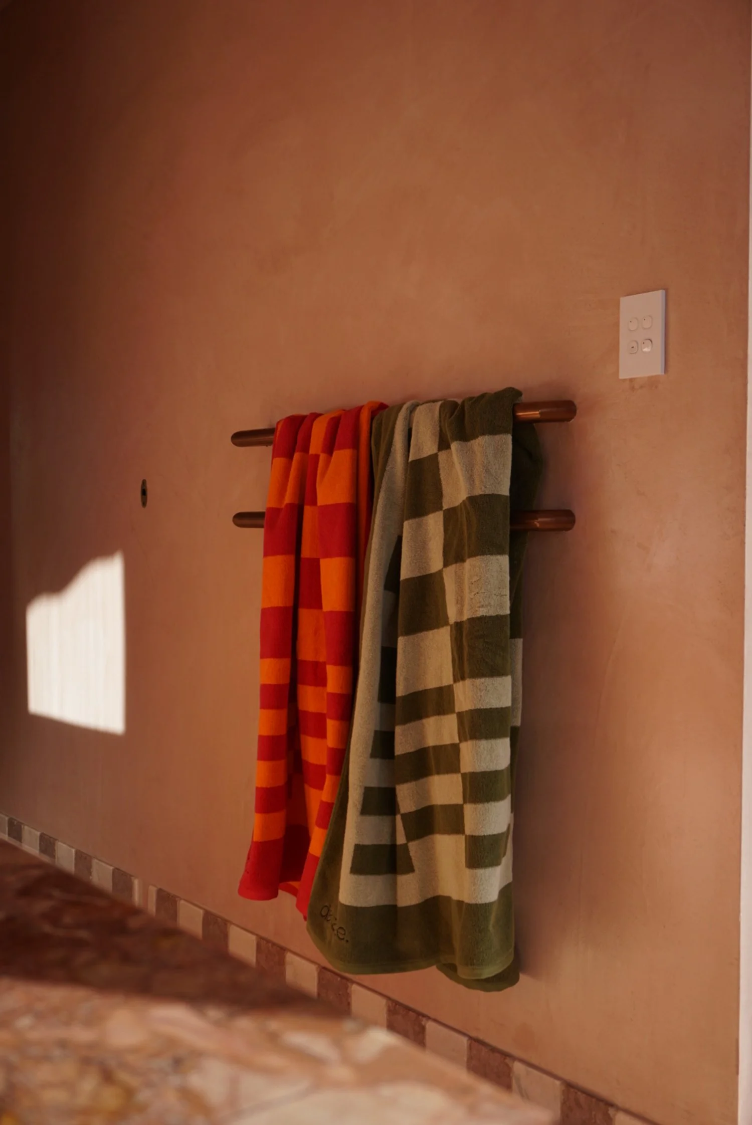 Two checkered towels hanging on a wall-mounted wooden towel rack, one with red and orange checkers, the other with green and beige checkers.