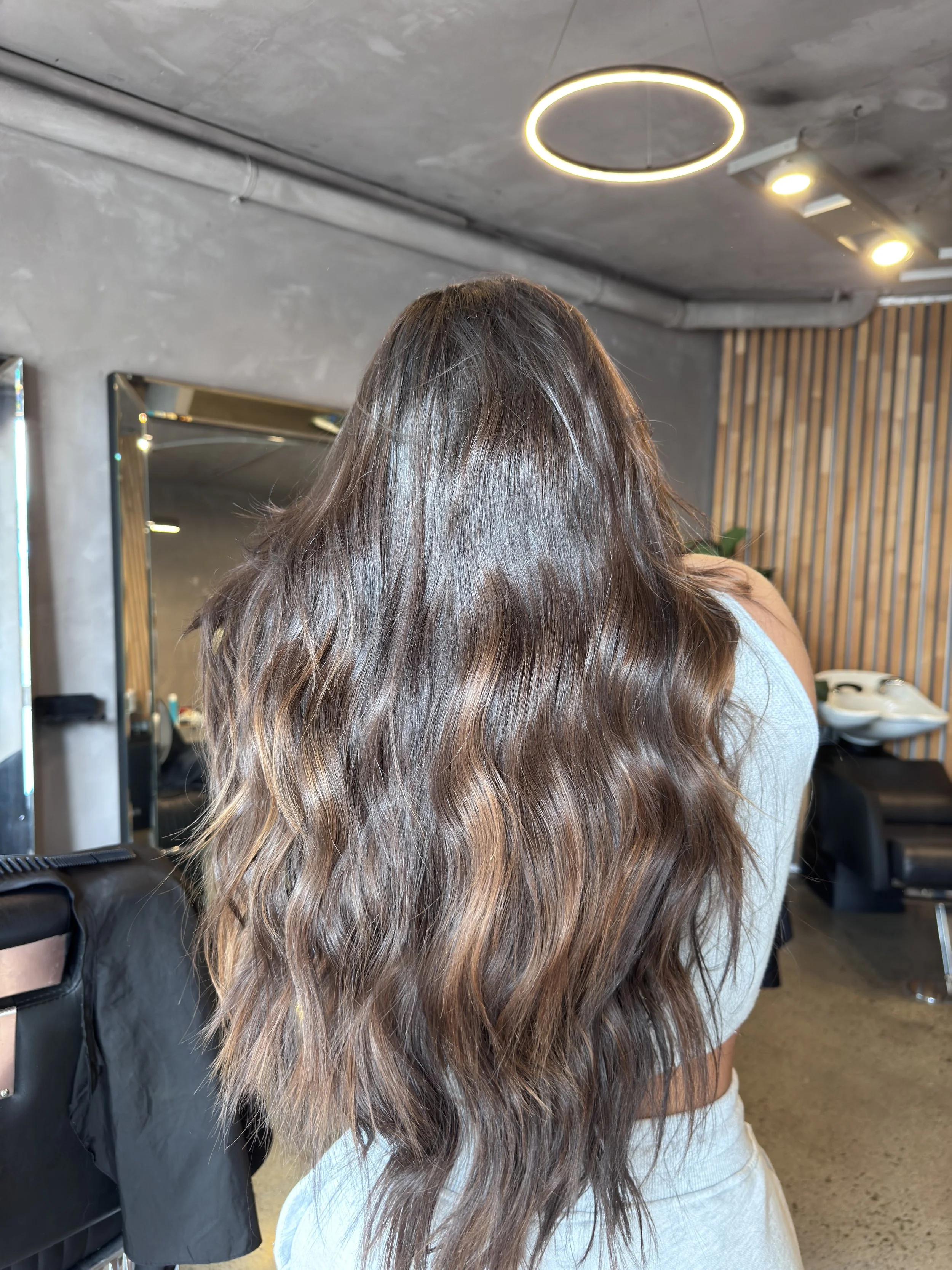 Back of a woman with long, wavy brown hair in a modern salon.