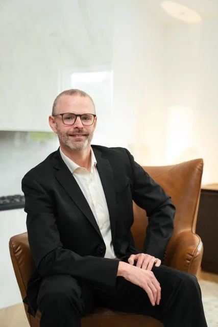 David Pipe, Guelph Ontario mortgage broker, seated in an office wearing a black suit jacket, white shirt and glasses.