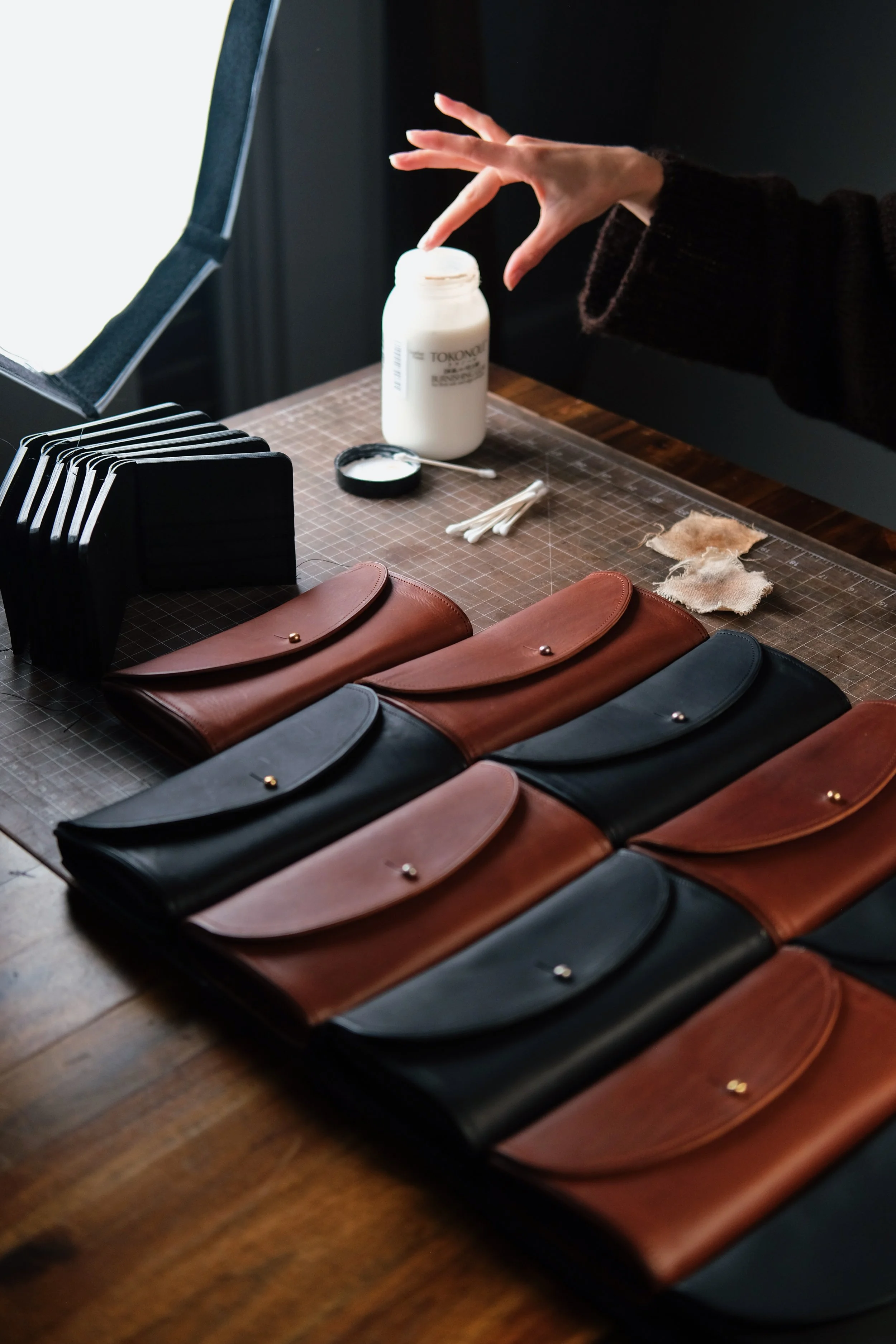 A workspace with several leather cluth wallets in shades of black and brown arranged on a wooden surface