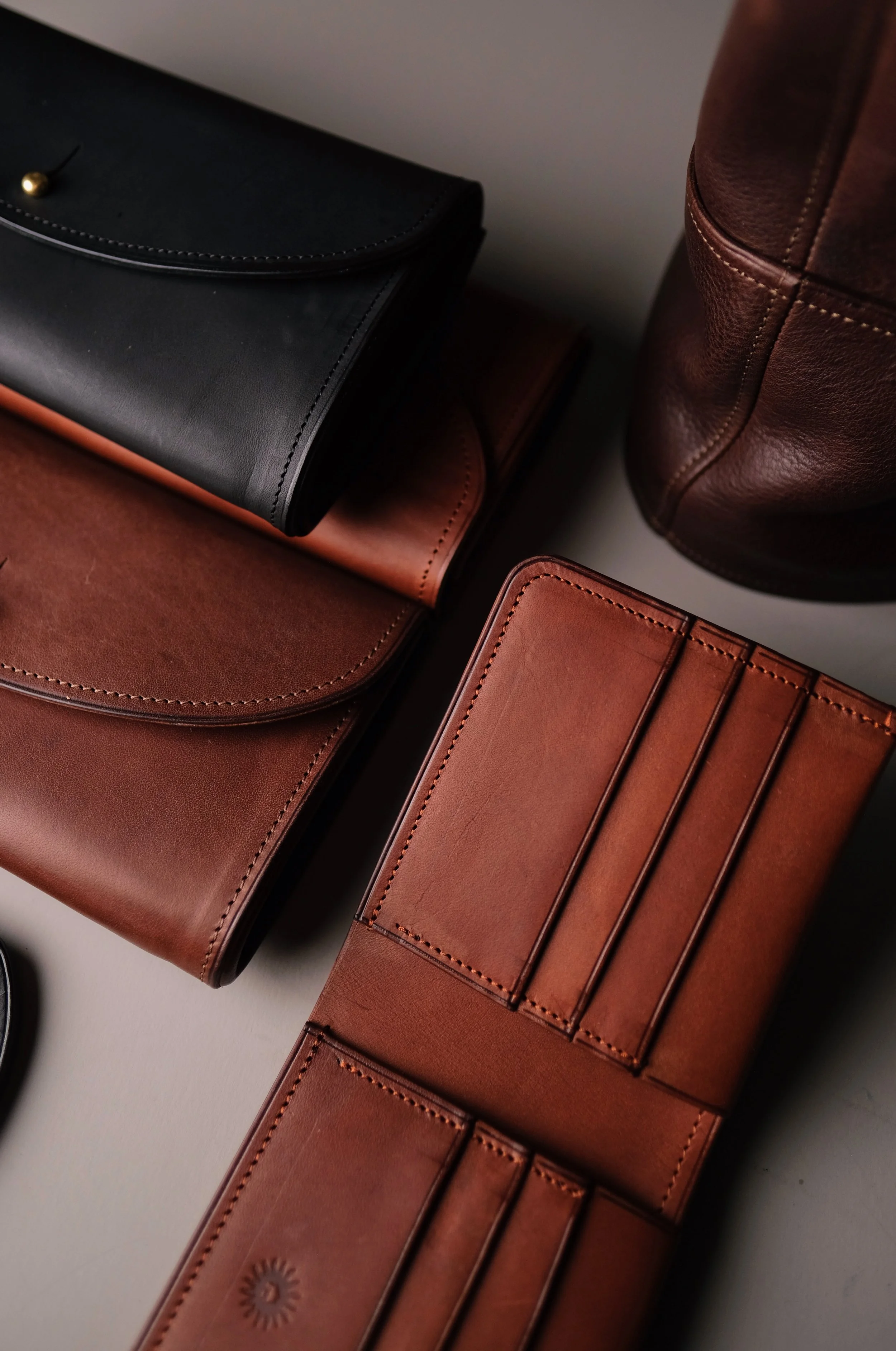 Close-up of four leather wallets or card holders in black, dark brown, light brown, and reddish brown, arranged on a white surface with the black wallet partially covering the others.