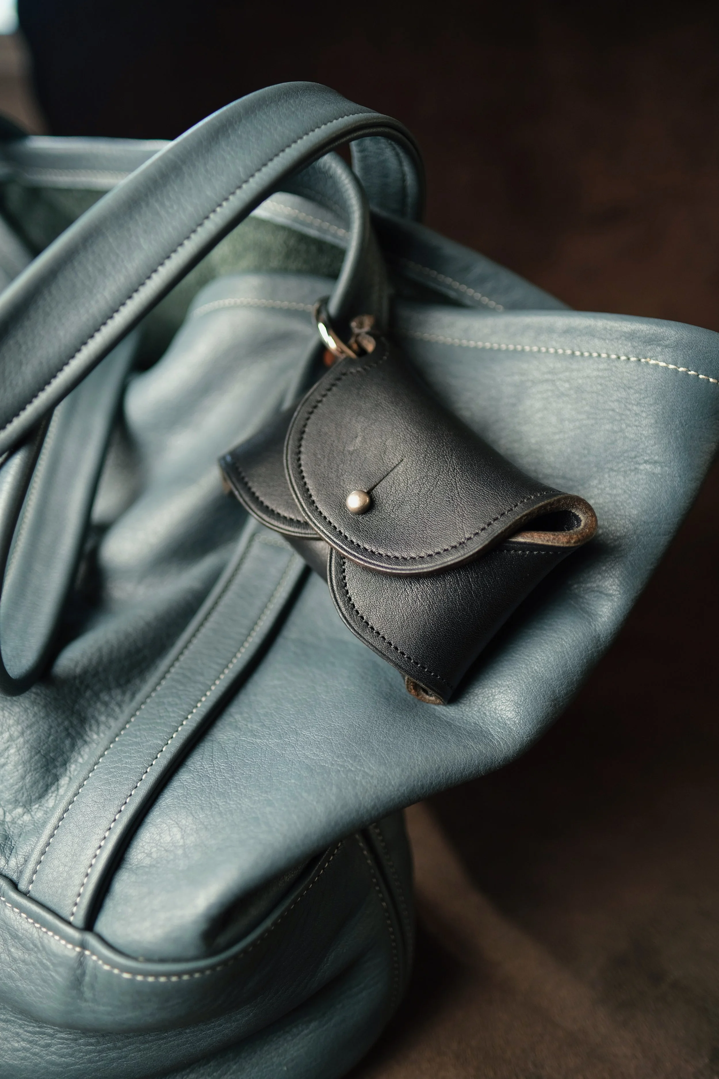 Close-up of a grey leather handbag with silver hardware and black envelope style wrist wallet
