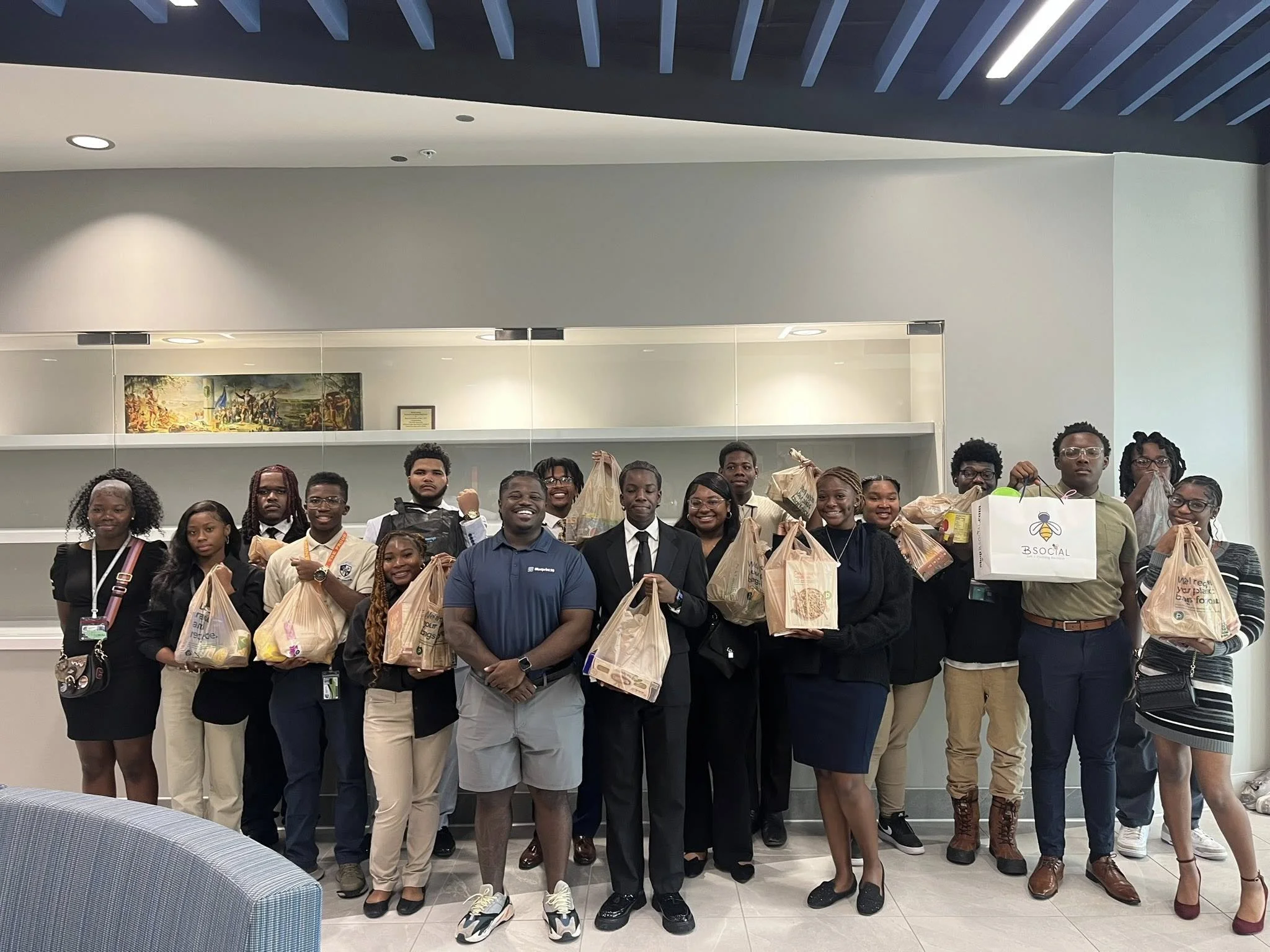 Group of people posing indoors, holding paper bags and some with certificates, in a modern building lobby.
