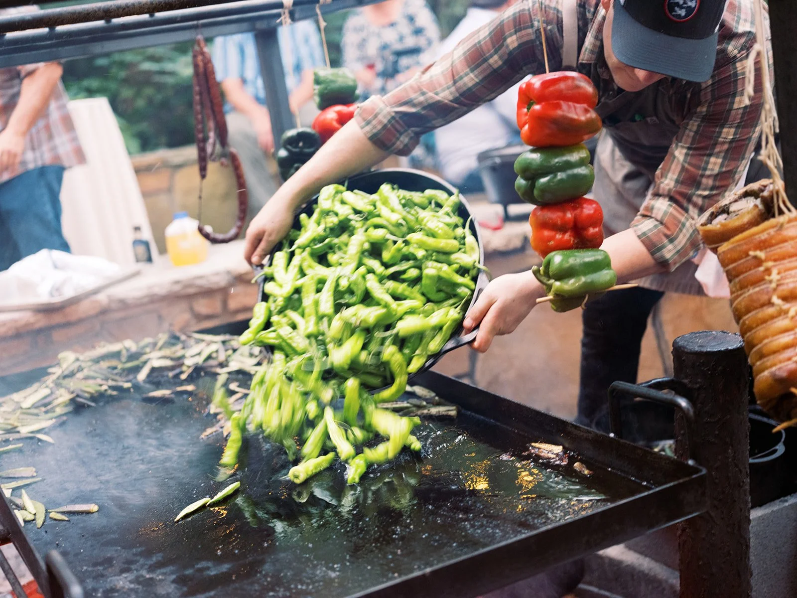 Chef adding fresh shishito peppers to a flat-top grill at an outdoor cooking event, lifestyle food photography by Cody Myers