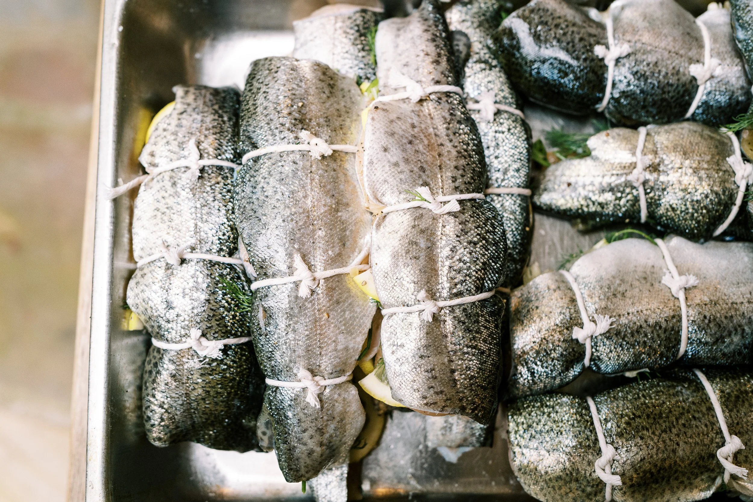 Multiple whole trout tied and seasoned in a sheet pan ready for cooking, food preparation photography by Cody Myers