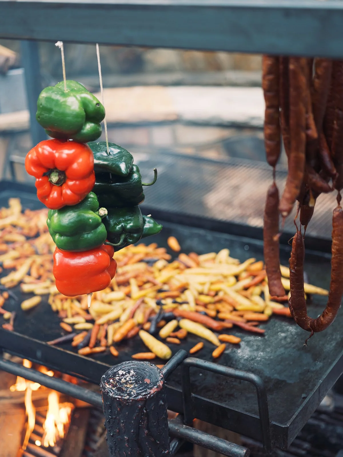 Red and green bell peppers on a skewer over an open flame grill, outdoor food photography by Cody Myers