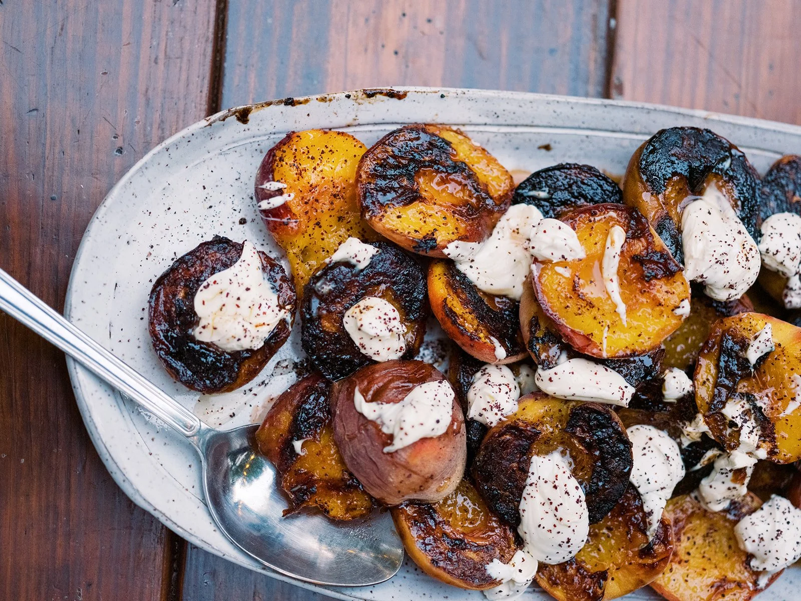 Grilled stone fruit with burrata and charred edges on a silver serving platter, food photography by Cody Myers