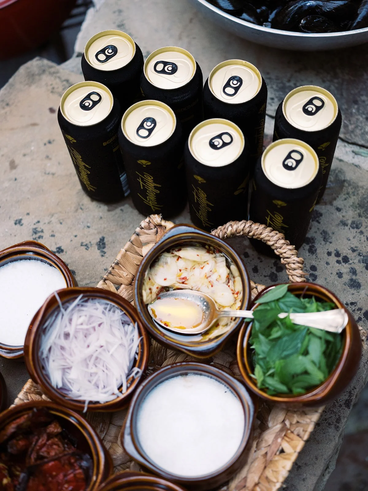Canned beers alongside small bowls of sauces and condiments at an outdoor dining spread, lifestyle food photography by Cody Myers