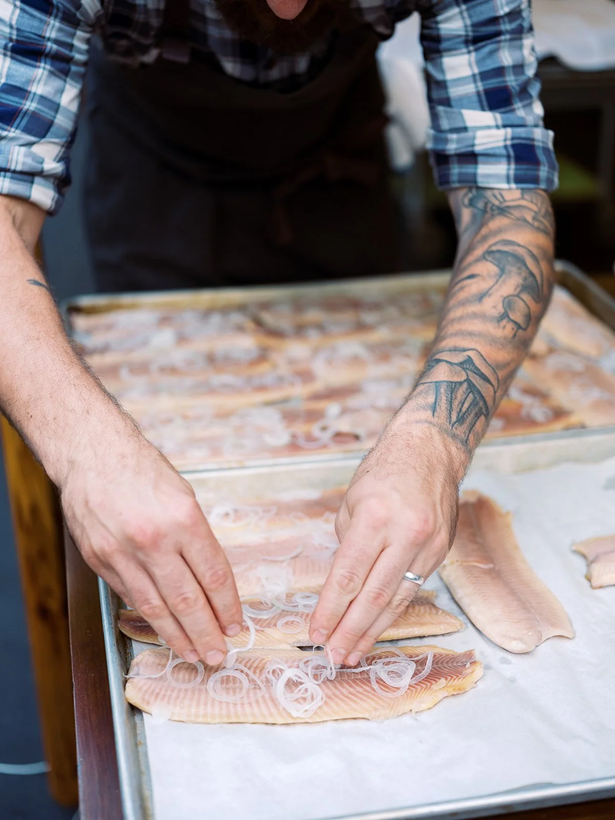 Tattooed chef preparing fresh fish on a cutting board, food preparation photography by Cody Myers