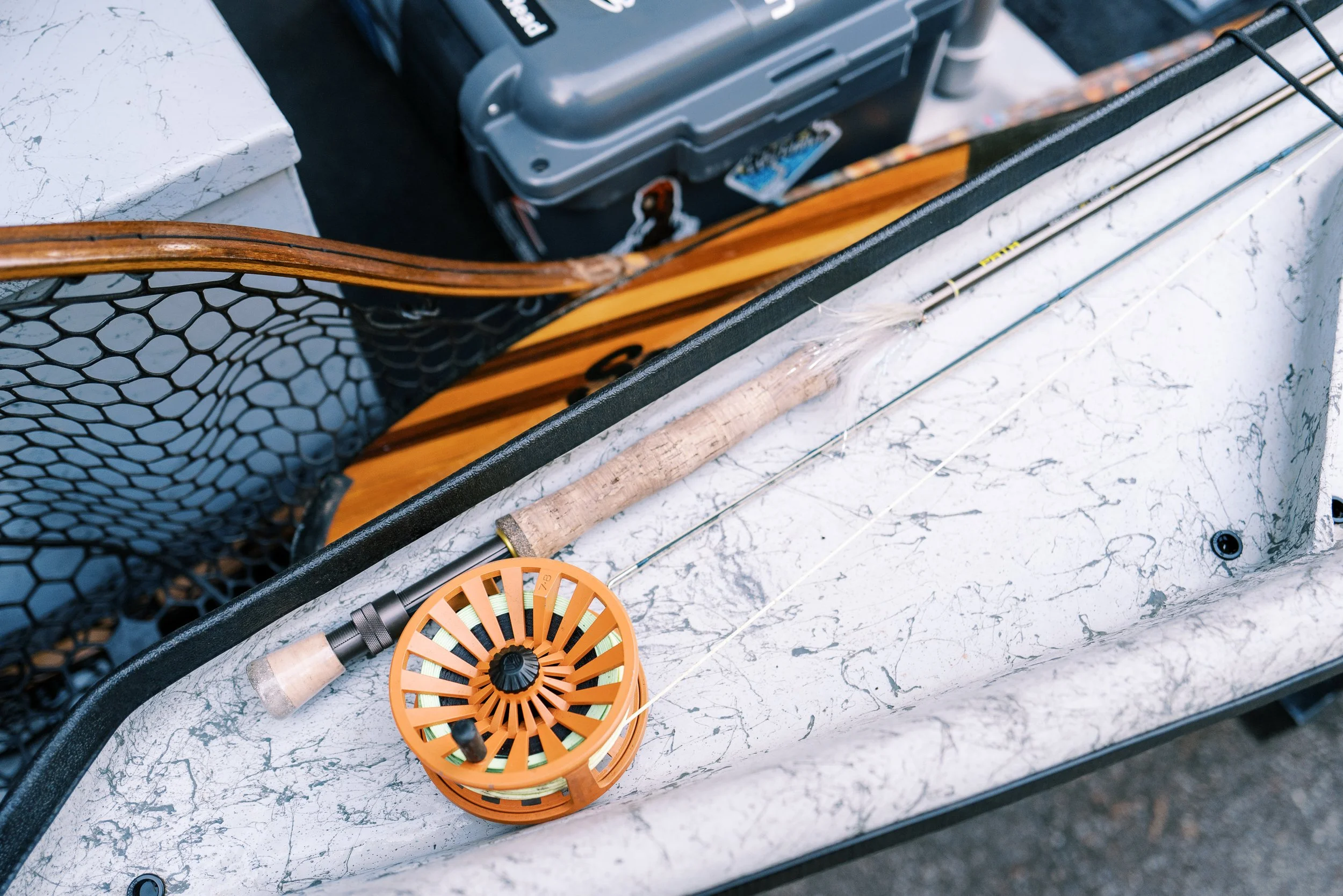 Fly fishing reel and rod resting on a boat alongside a net, outdoor lifestyle photography by Cody Myers