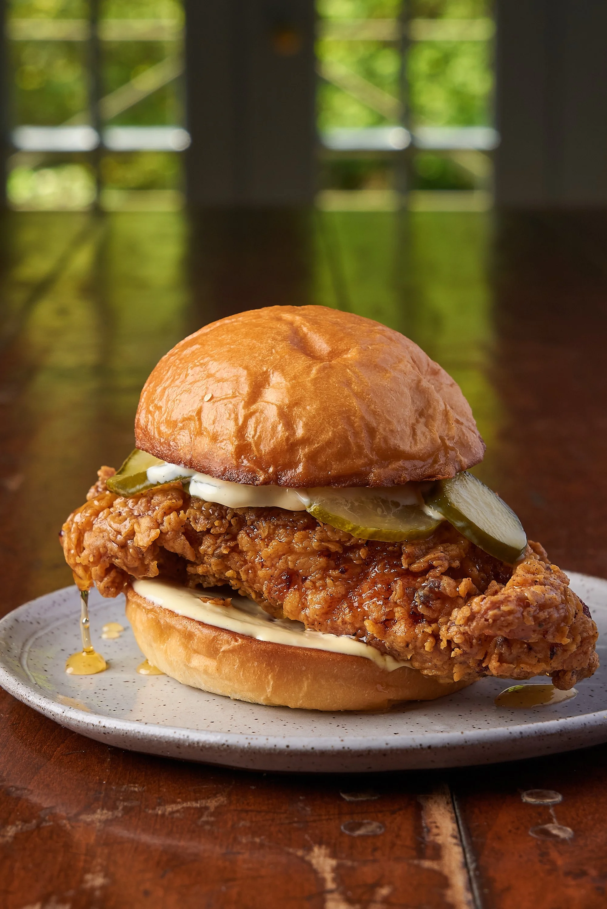 Crispy fried chicken sandwich on a brioche bun plated on a wooden table, food photography by Cody Myers