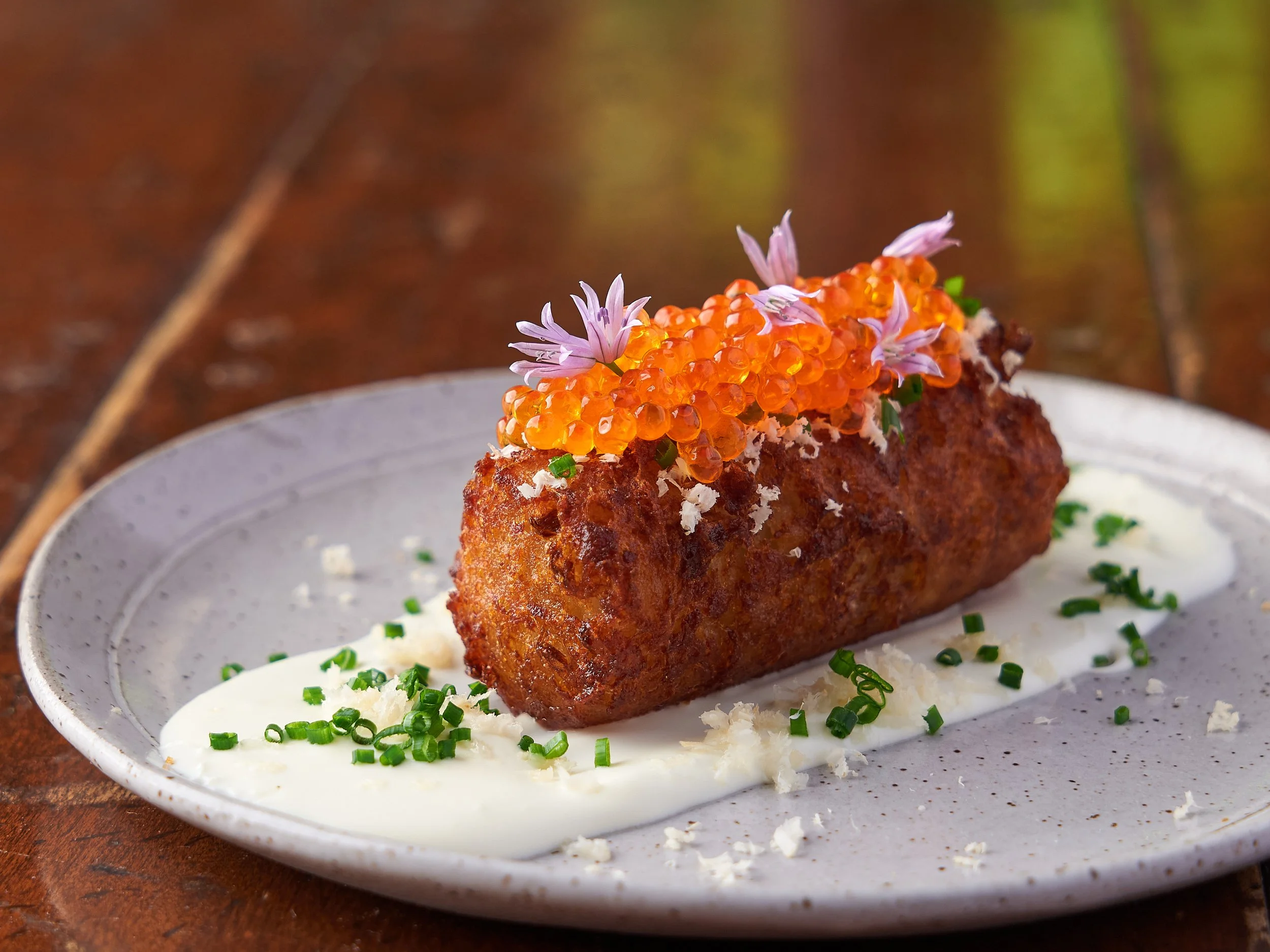 Crispy croquette topped with salmon roe and edible flowers on a cream sauce, fine dining food photography by Cody Myers