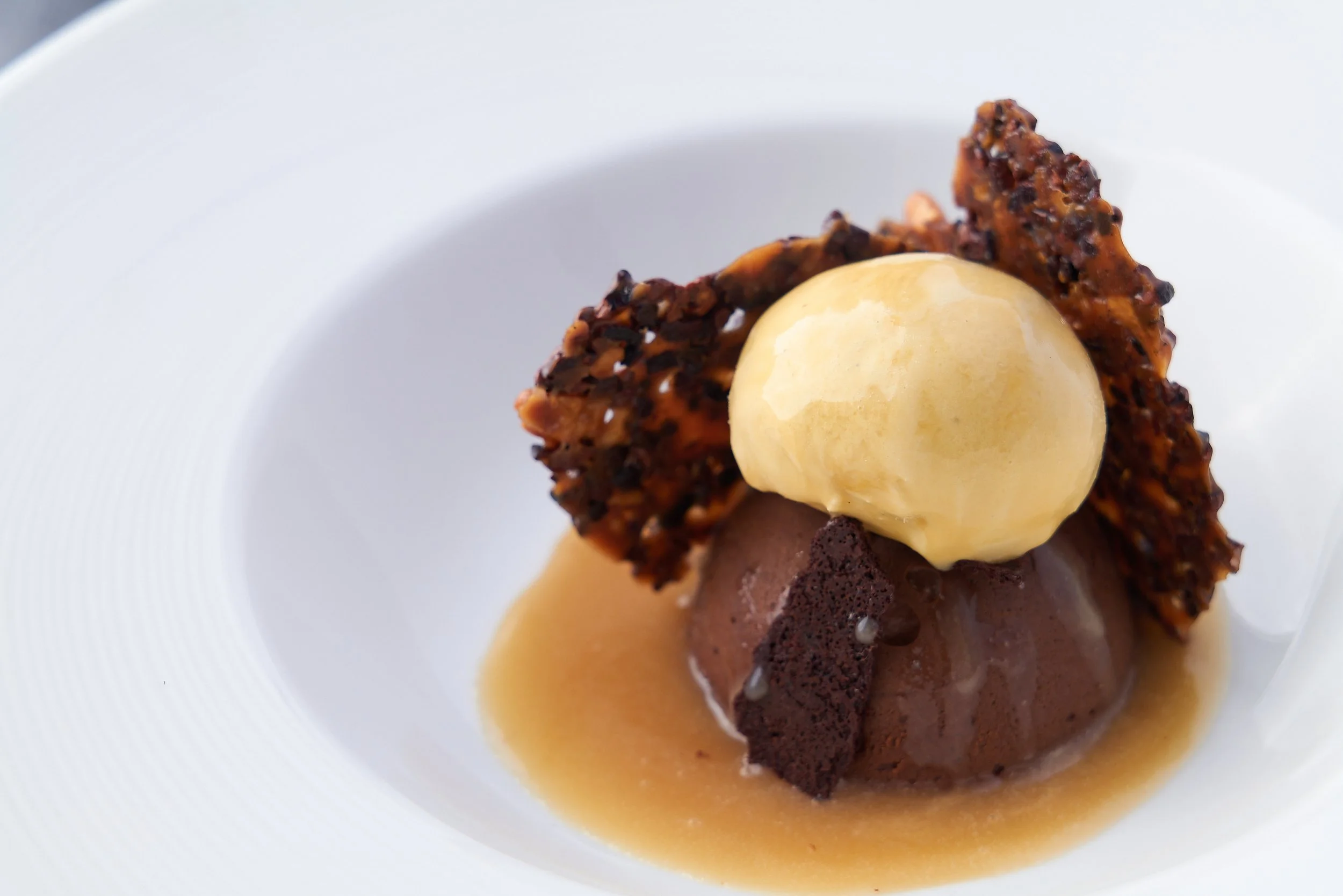 Chocolate dessert with vanilla ice cream and caramel sauce on a white plate, fine dining food photography by Cody Myers