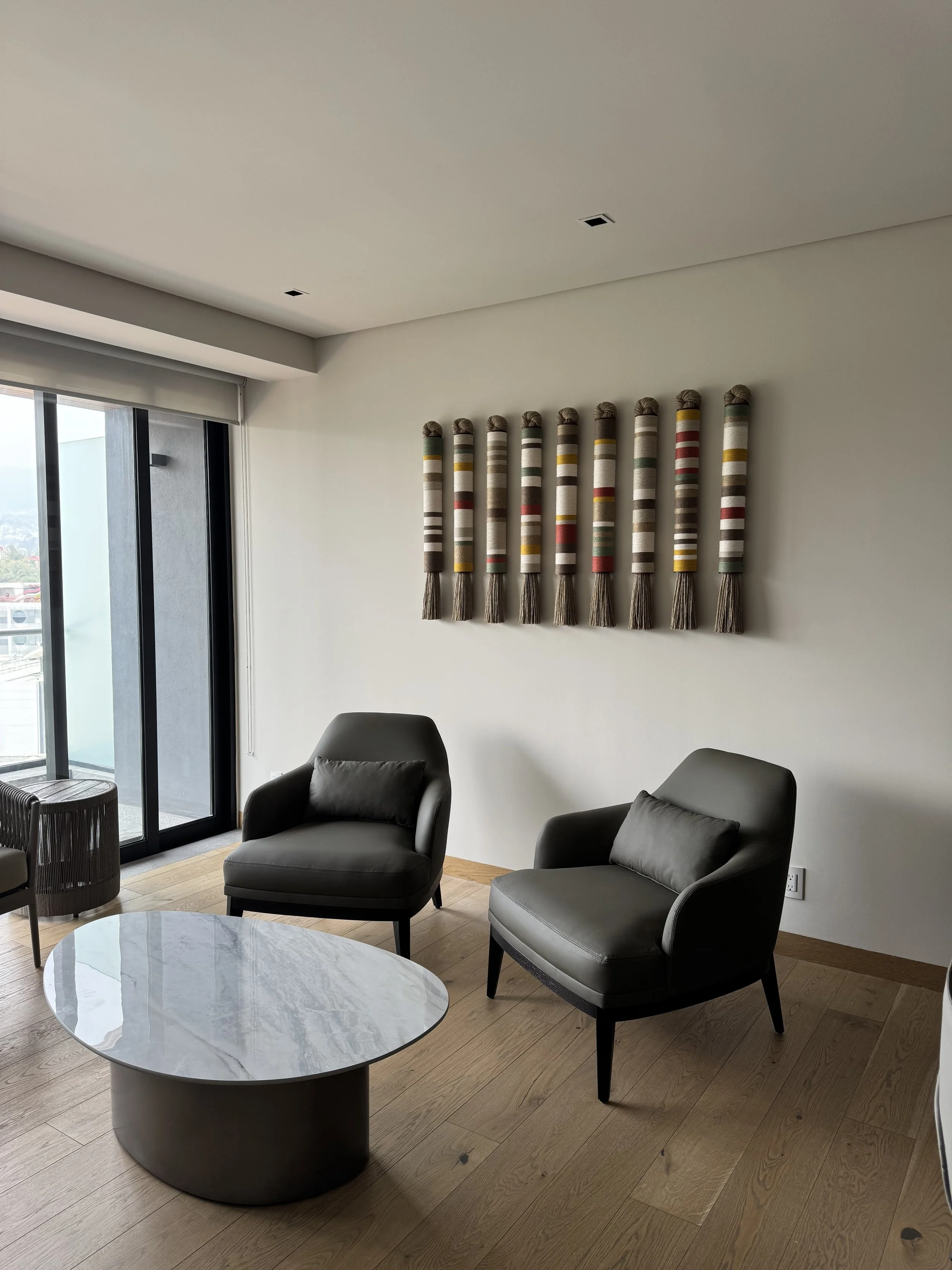 Sala de estar con dos sillones negros, una mesa de centro de mármol y decoraciones en la pared.