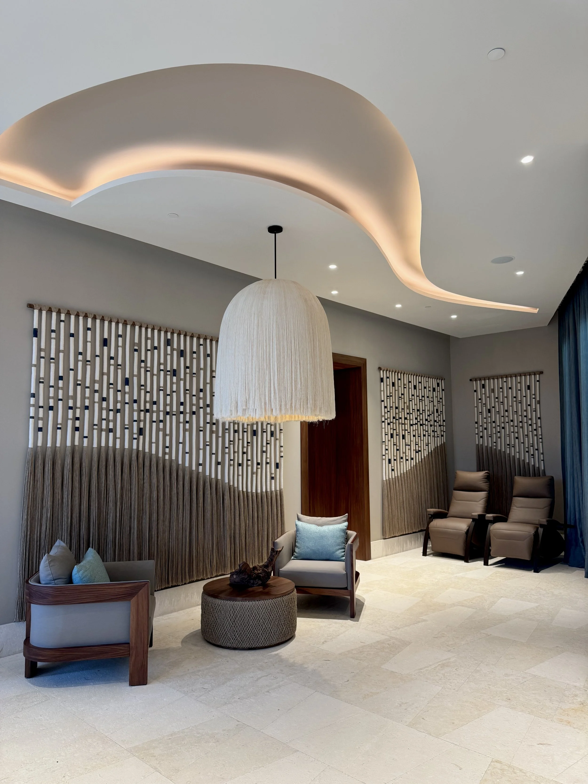 Sala de estar moderna con sillas reclinables, un sillón pequeño, una lámpara colgante, cortinas con diseño de rayas y una pared decorada con textiles