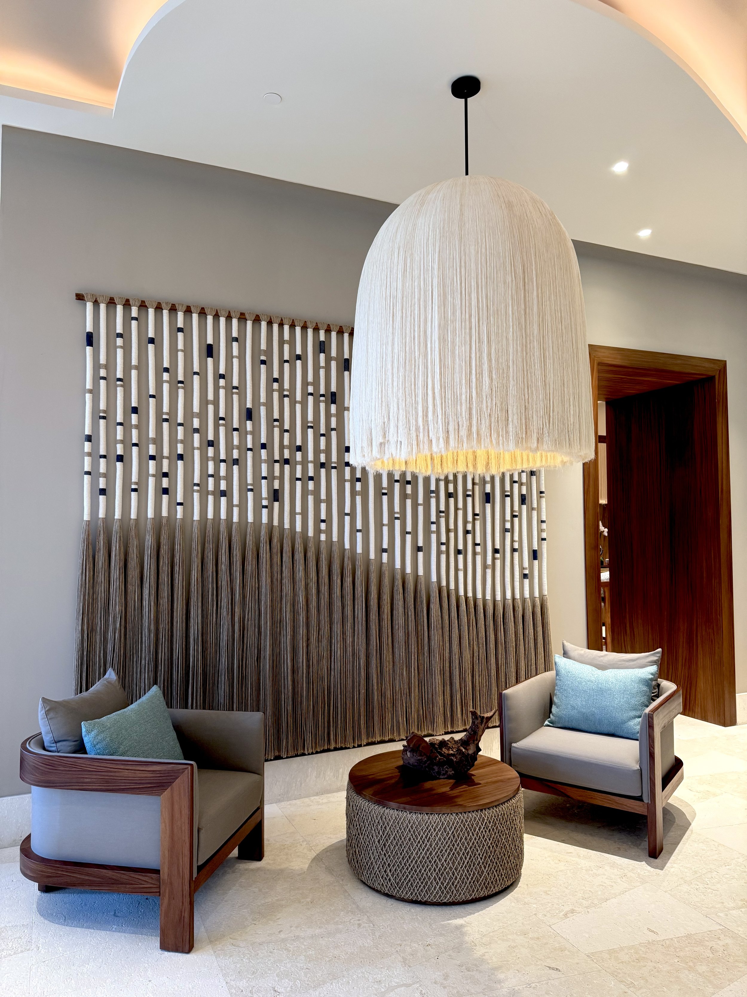 Área de descanso con sillones, mesa rústica, lámpara de techo decorativa y pared con cortinas de barrotes verticales, en interiores elegantes.
