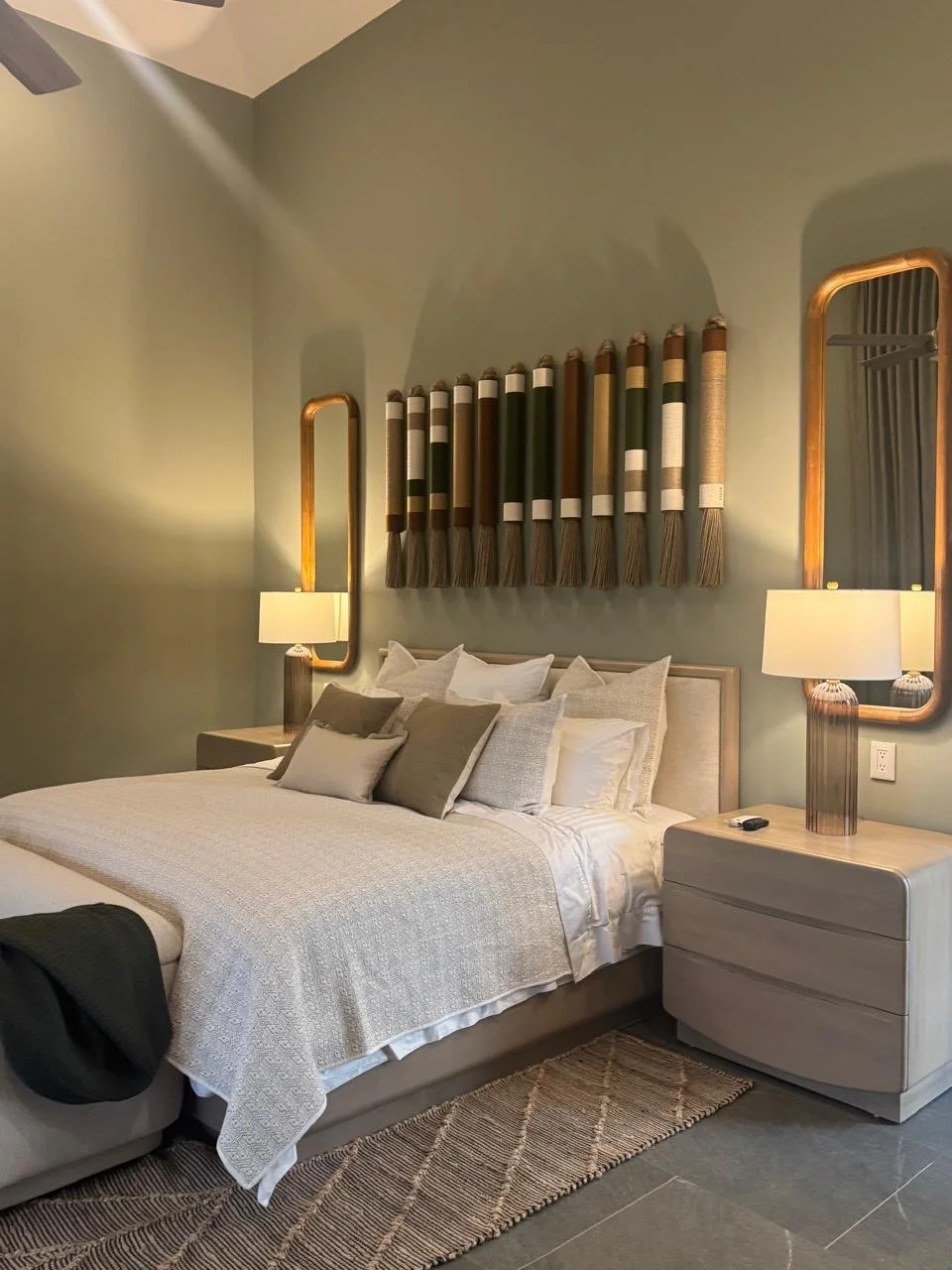 Dormitorio con cama grande, cabecera con decoración de textiles colgantes, dos mesitas de noche con lámparas y espejos