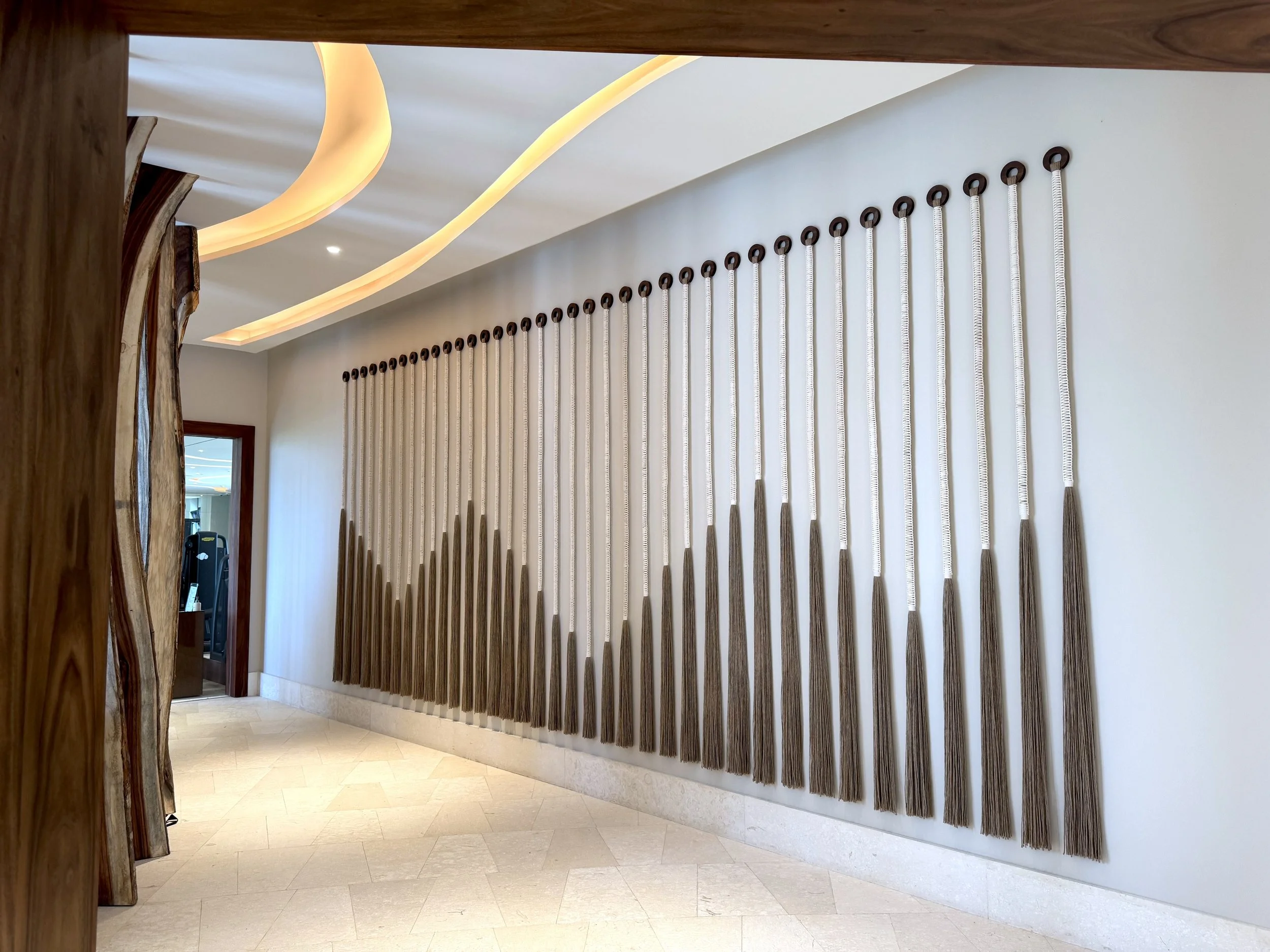 Pared decorativa con cuerdas que caen desde argollas de madera colgadas en un espacio interior moderno.