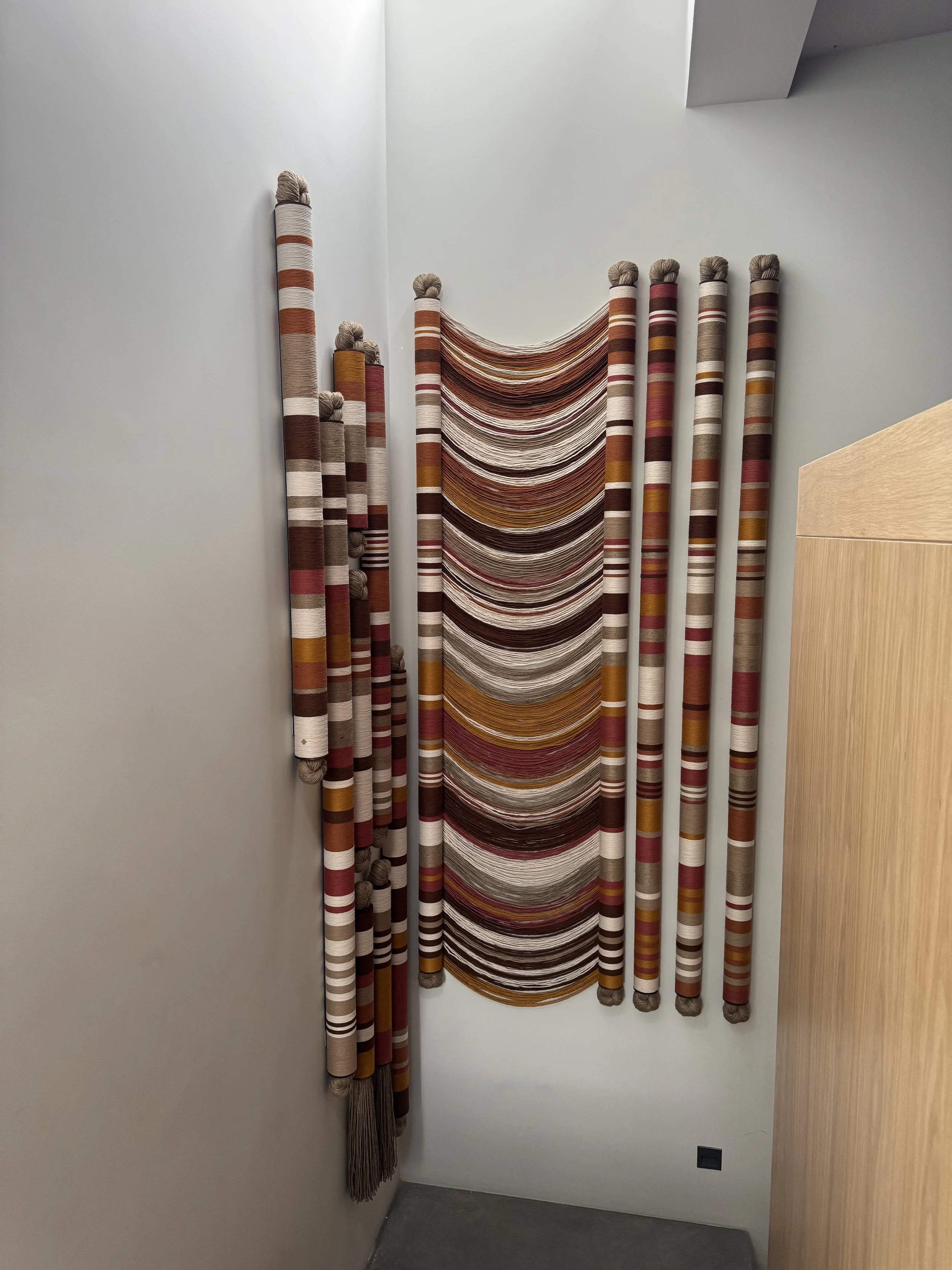Varias piezas de tapetes tejidos de diferentes colores y patrones, colgados en la pared de una tienda de alfombras.