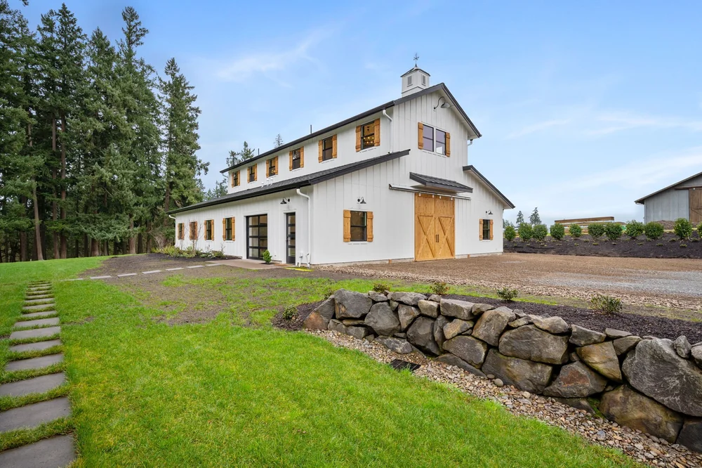 Side and front of the barndominium beside a lawn and stone retaining wall.