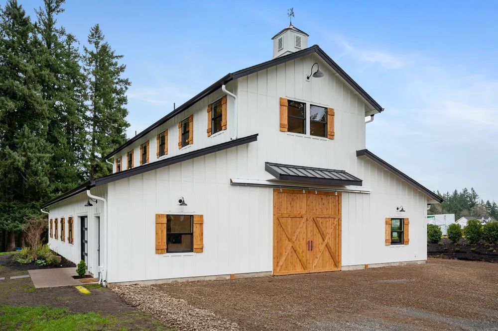 Angled front view of the white barn with cedar doors and a metal awning.