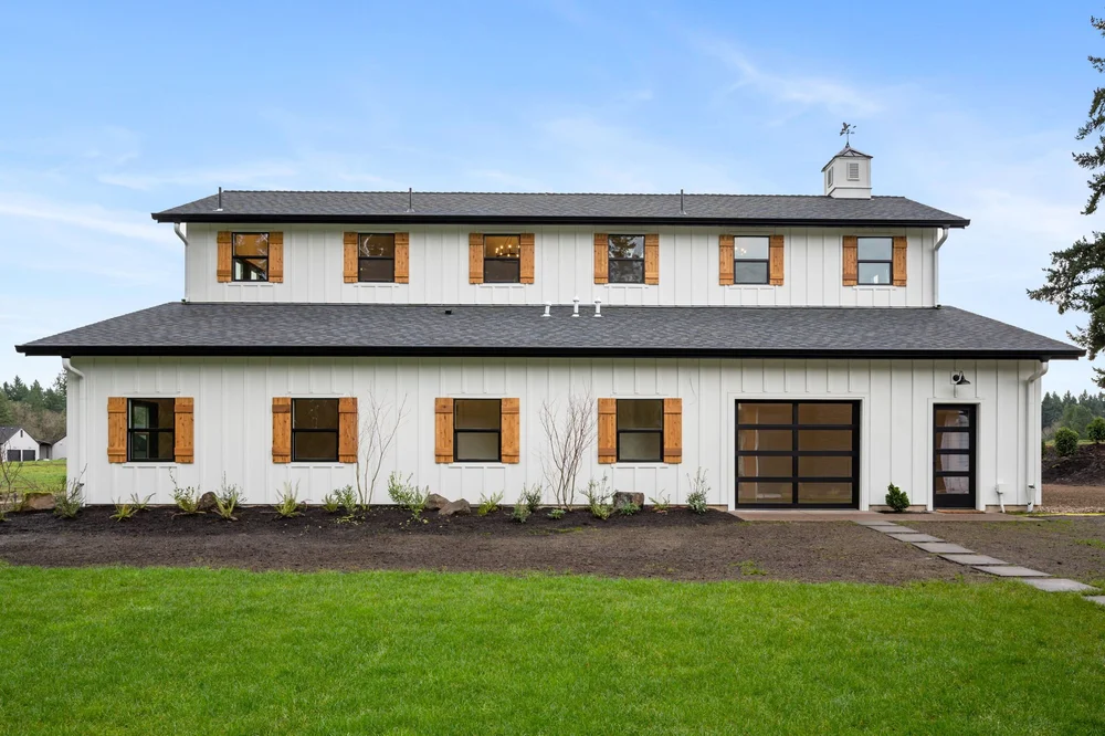 Long white barn facade with cedar shutters facing the lawn.