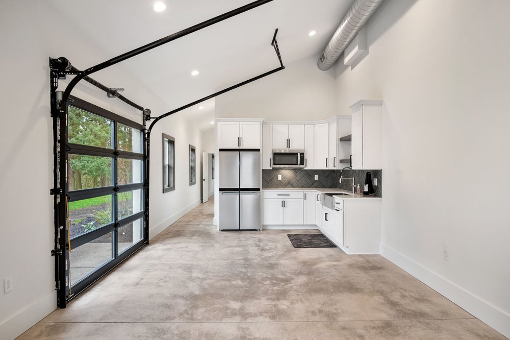 Kitchen and adjacent open space with a glass garage door bringing in daylight.