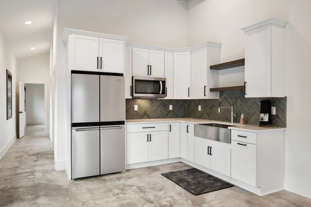 Full kitchen with white cabinets, stainless steel appliances, and a dark herringbone backsplash.