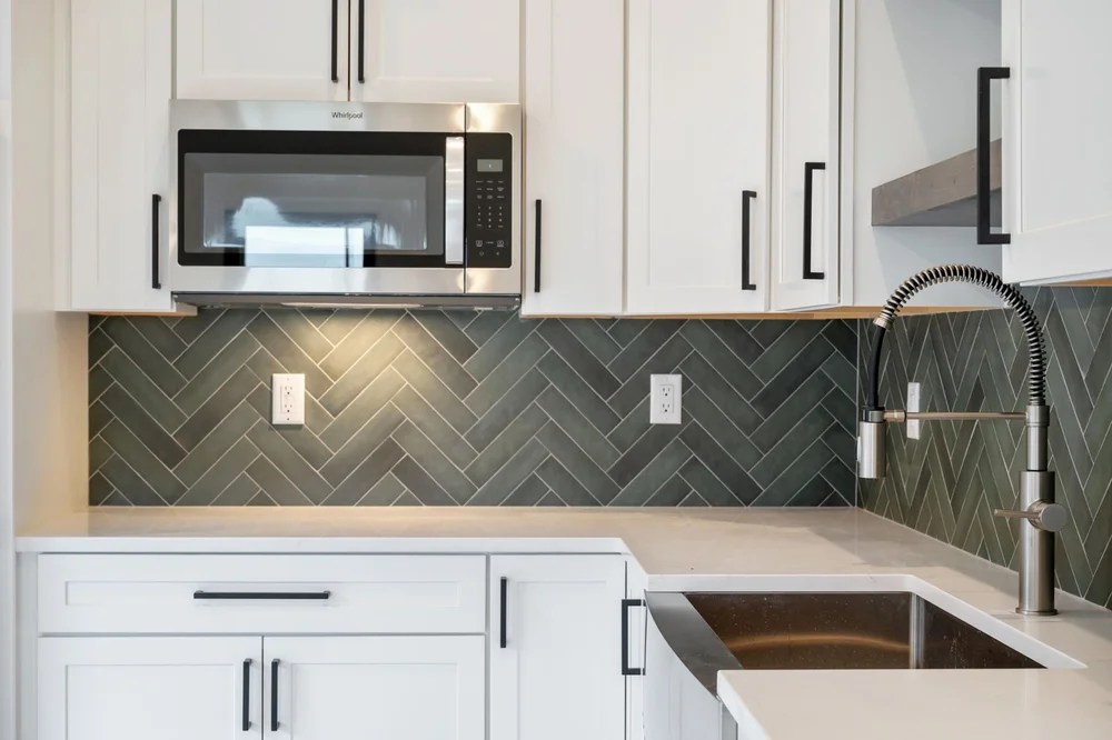 White cabinetry, a dark herringbone backsplash, and a sink with a high-arc faucet.