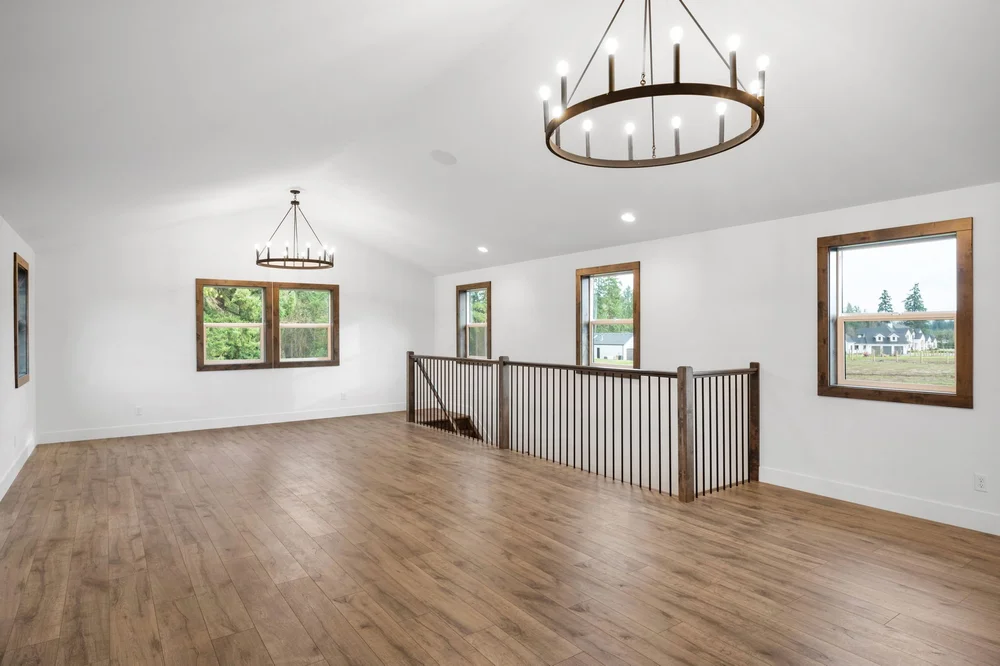 Light-filled loft with wood floors, a circular chandelier, and a railing around the stairs.