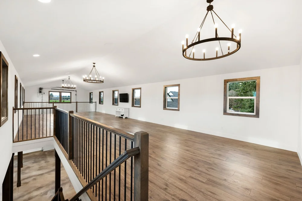 Open loft framed by windows, wood trim, and dark stair balusters.