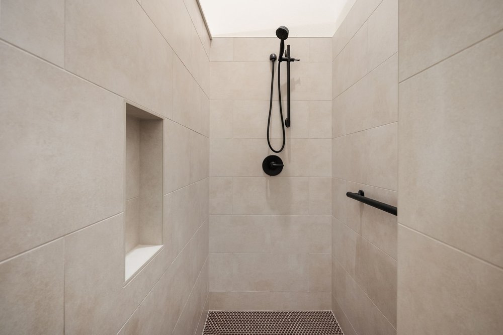Tiled shower with a recessed niche and dark fixtures.