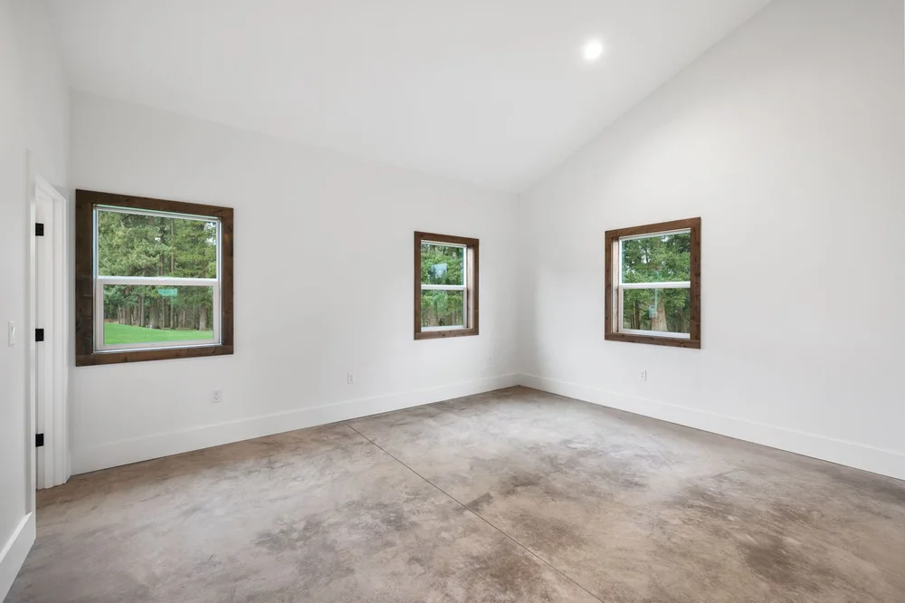 Unfurnished bedroom with two windows, wood trim, and white walls.