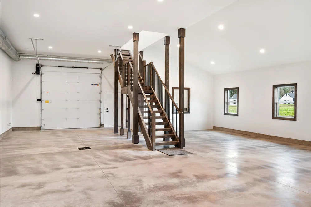 Open concrete floor beneath the loft with wood posts and a large garage door.