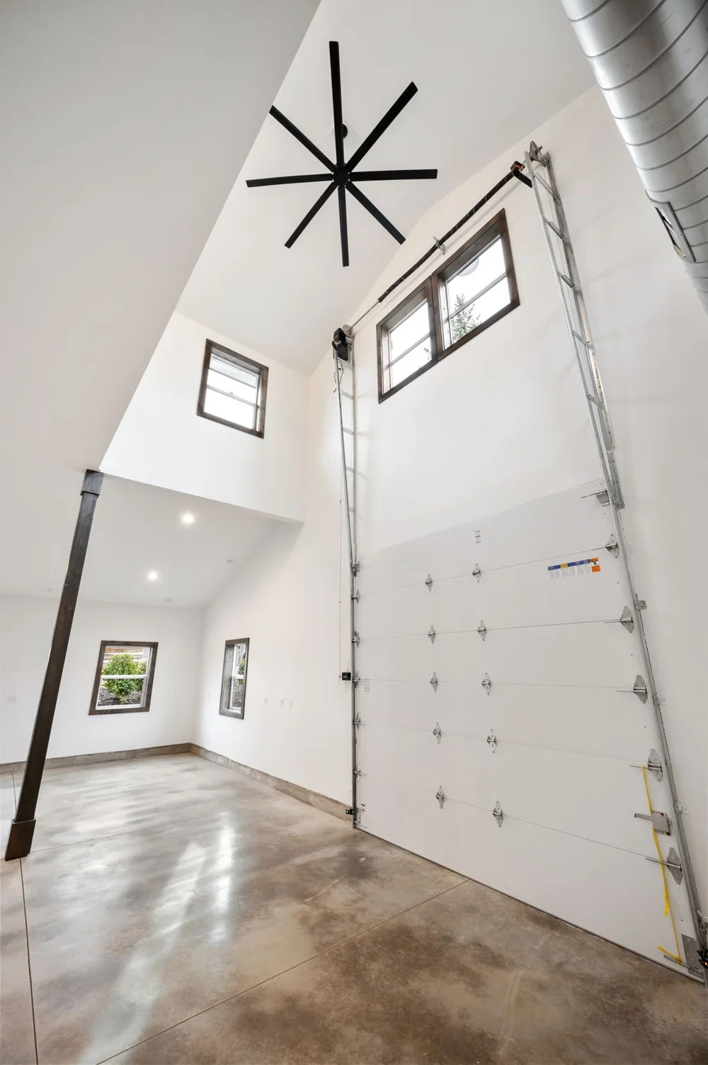 Tall main-floor interior showing the garage door, high ceiling, and large fan.