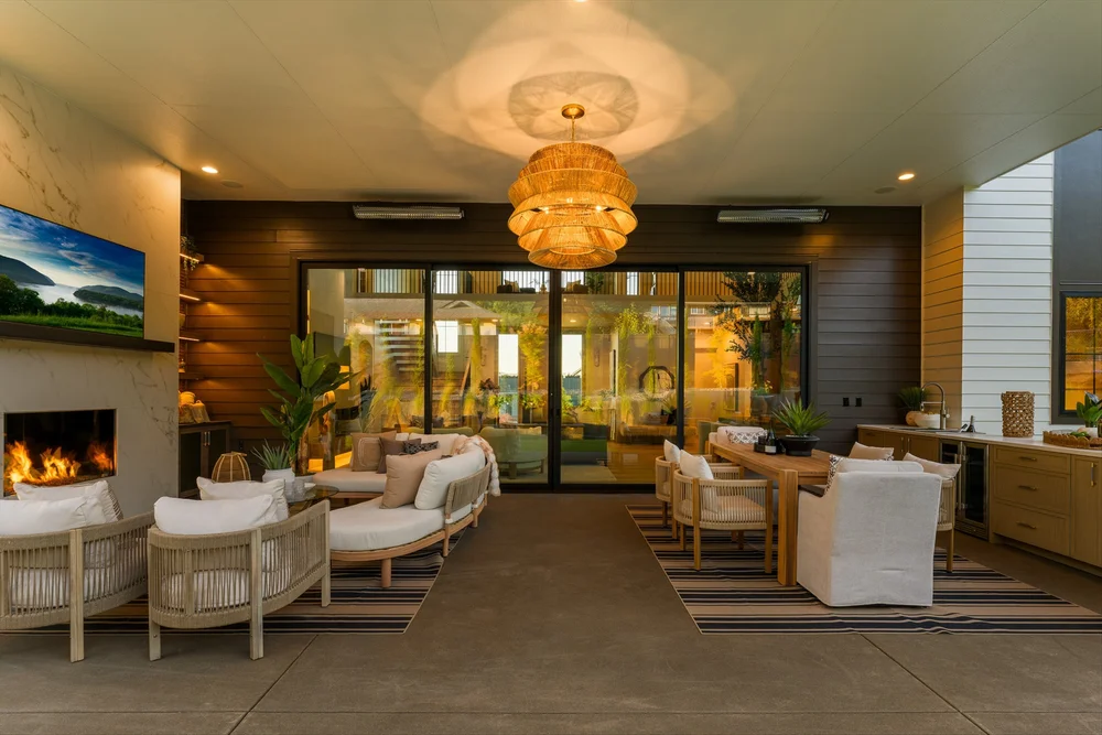 A covered entertaining area with lounge seating, a dining table, and an outdoor kitchen