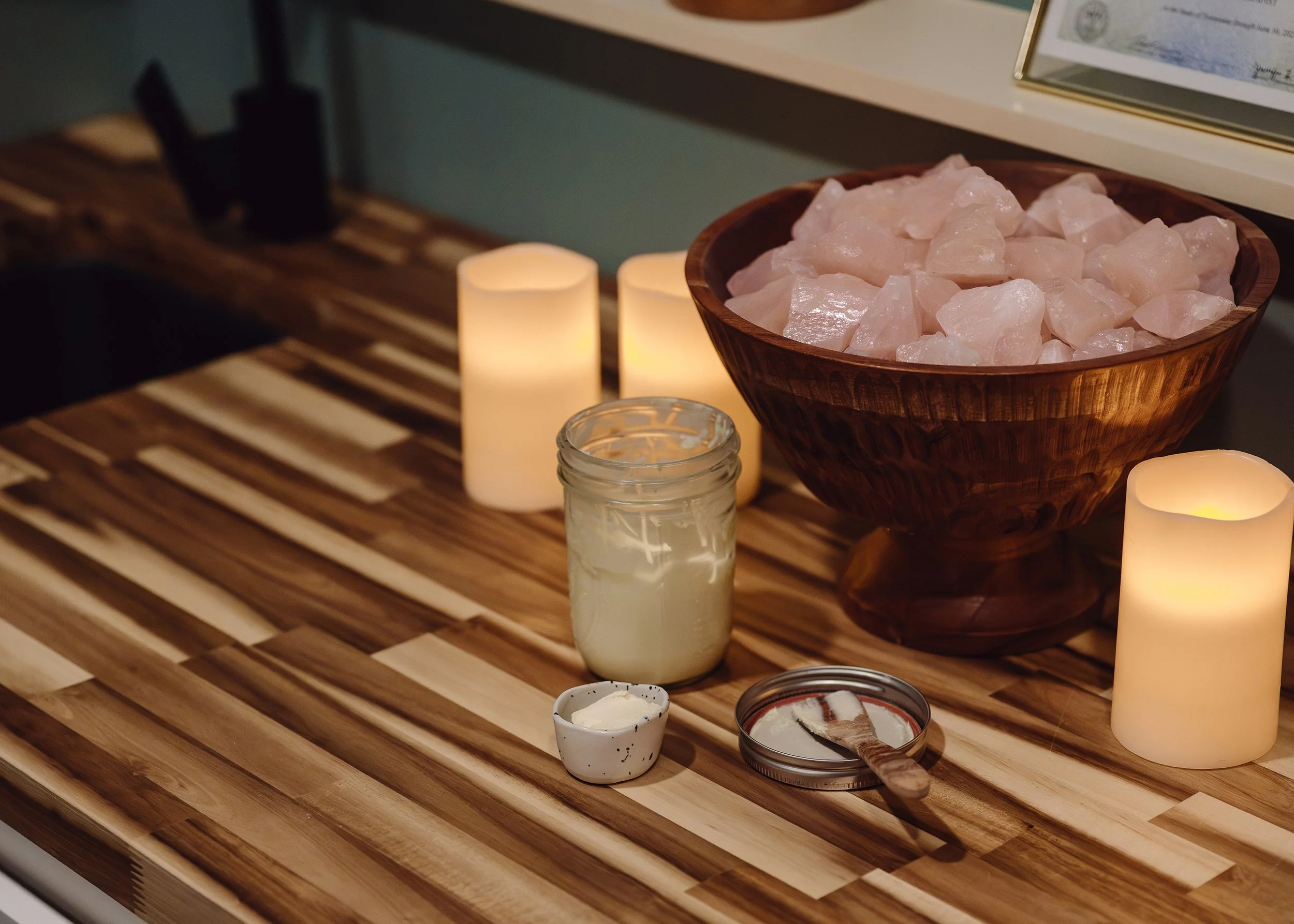 body butter in a mason jar with some spooned out into a pinch cup next to a bowl of raw rose quartz