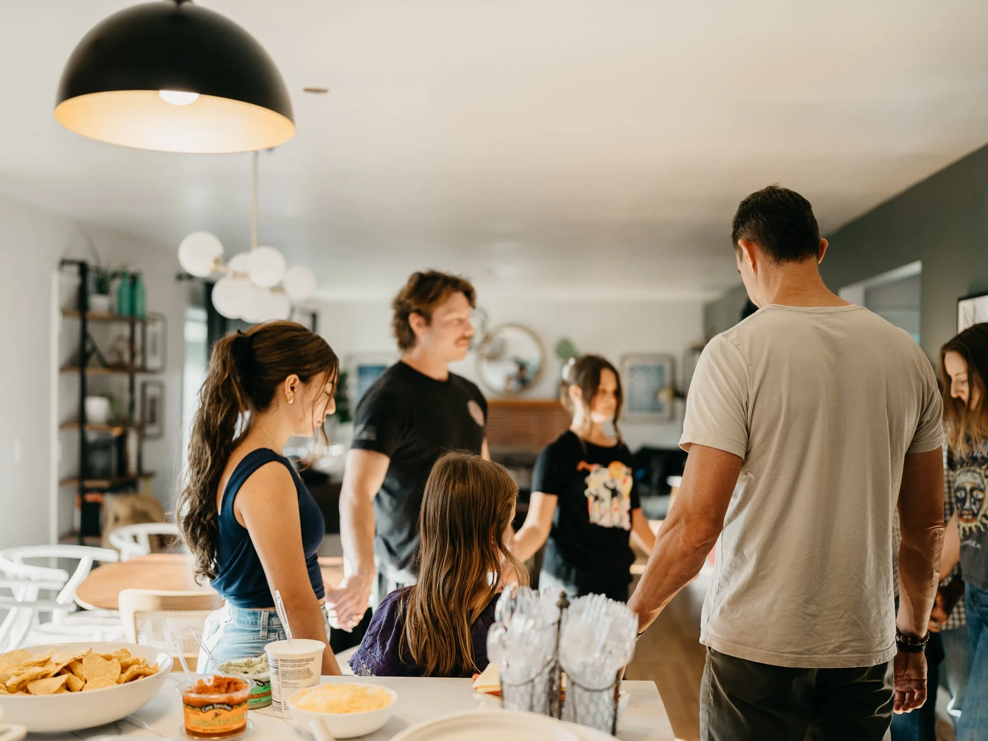 Community at Sonoma Collective. A Group of people gathered around a kitchen island, engaging in conversation, with food and drinks on the counter.