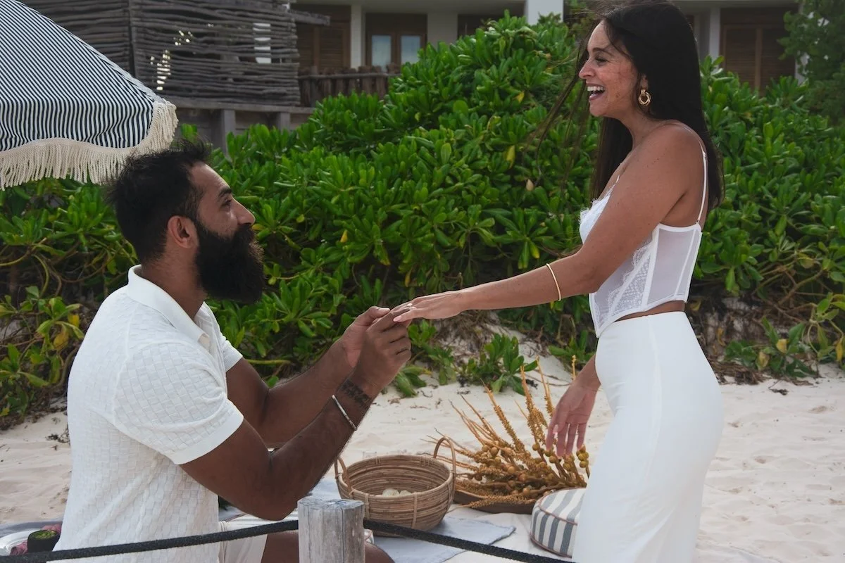 A man kneeling and proposing to a woman on a beach with a proposal picnic on Tulum Beach. 