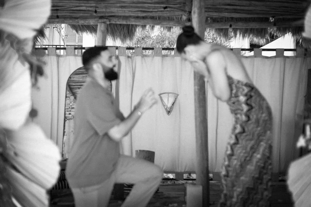 Black and white photo of a man kneeling in front of a woman inside a rustic setting, possibly a marriage proposal in Tulum.