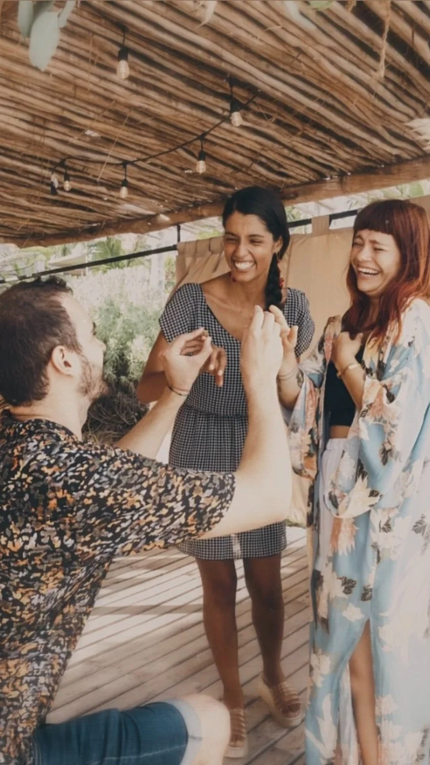 Man proposing to a woman while another woman watches in Tulum, under a wooden pergola.