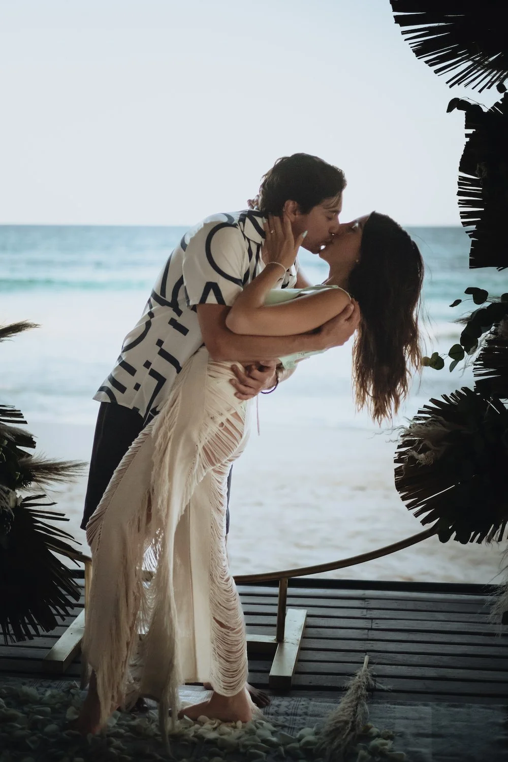 Couple kissing by the beach in Tulum with tropical decoration.