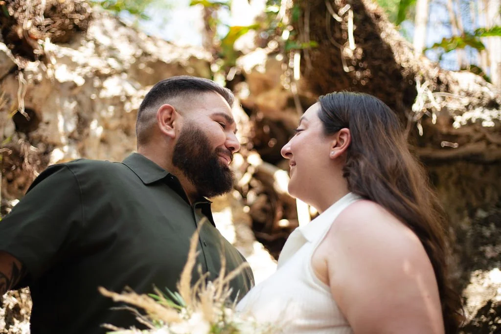 A couple smiling at each other in an outdoor, natural setting, it's their marriage proposal in a Cenote in Tulum.